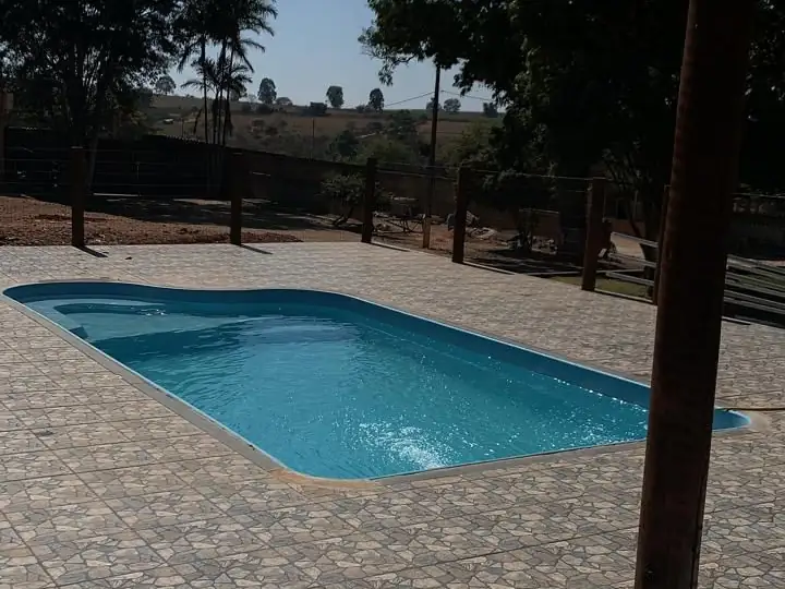 Piscina ao ar livre com piso de pedra, cercada por mourões de madeira e árvores